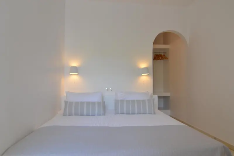 Une chambre lumineuse avec un grand lit blanc et des coussins gris.