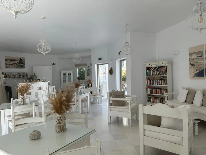 Une salle lumineuse et minimaliste avec des tables et des chaises blanches, des luminaires décoratifs et un coin lecture.