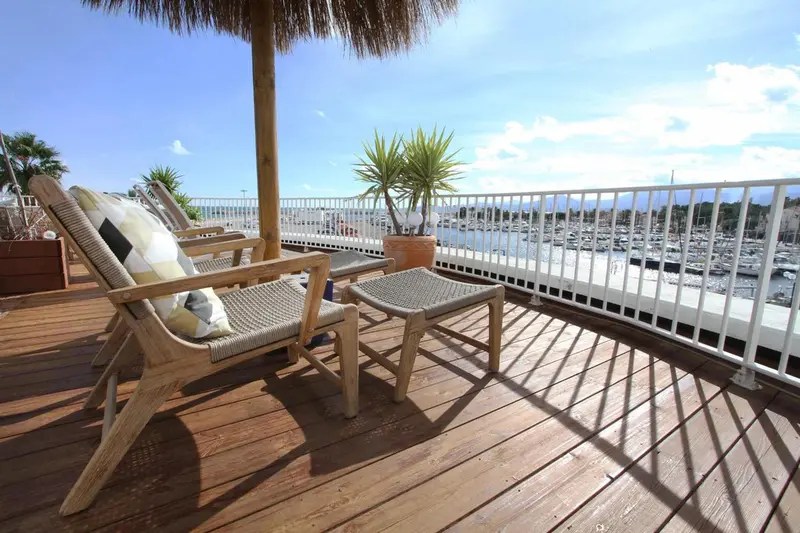 Terrasse en bois avec chaises longues et vue sur un port de plaisance.