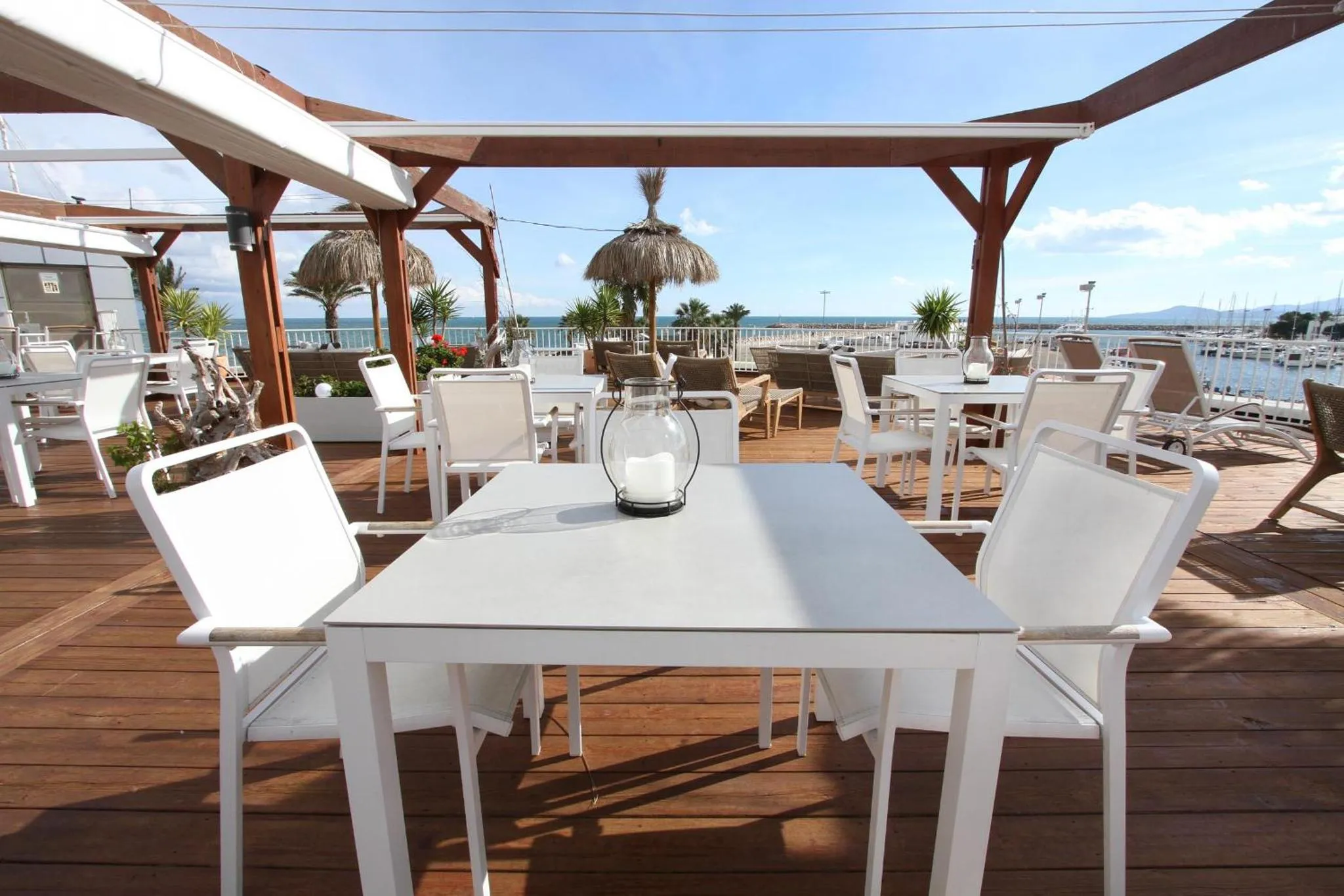Terrasse ombragée avec tables et chaises blanches face à la mer.