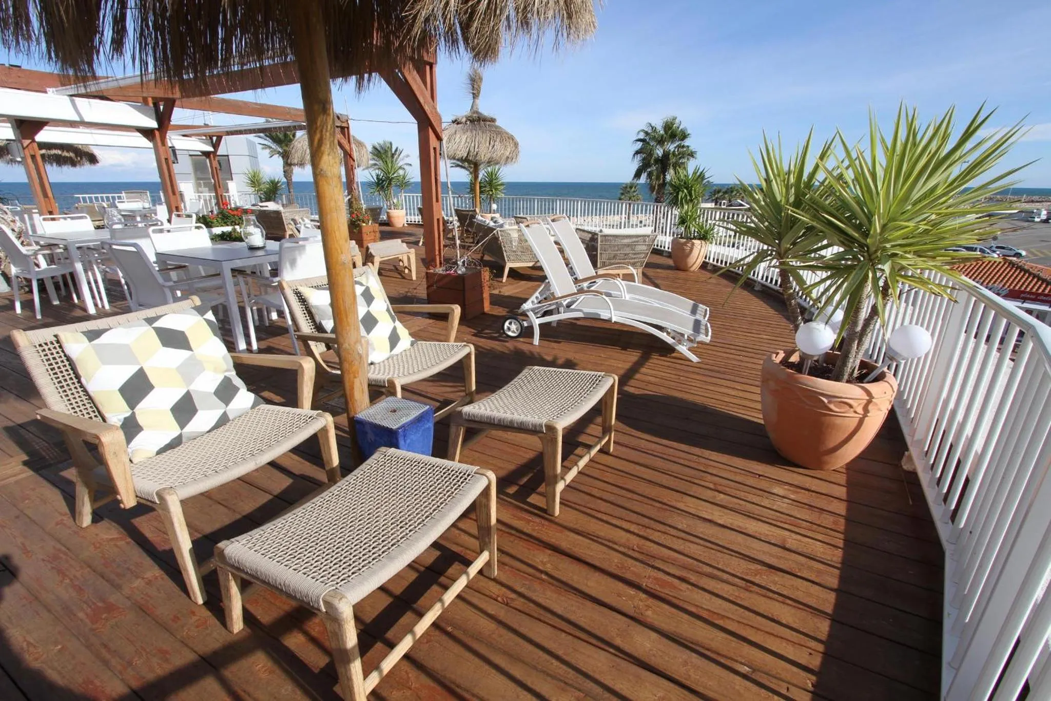 Terrasse en bois avec transats et mobilier de jardin face à la mer.