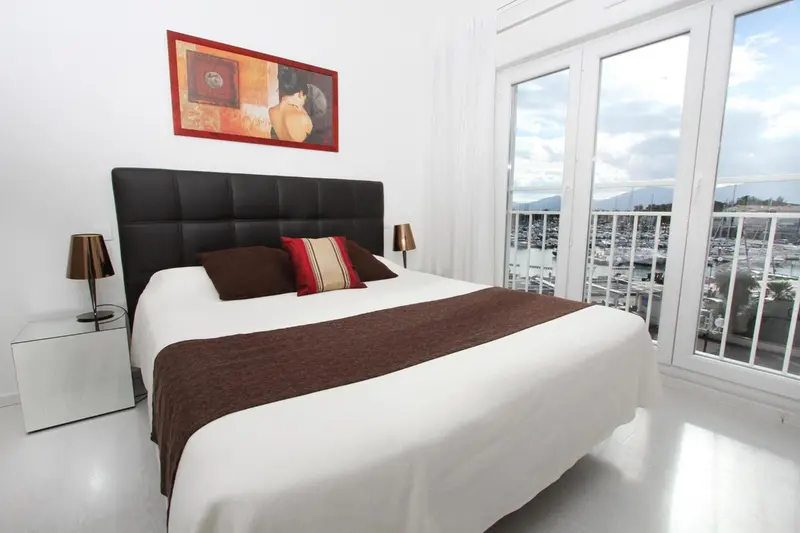 Une chambre lumineuse avec un grand lit et une vue sur le port.