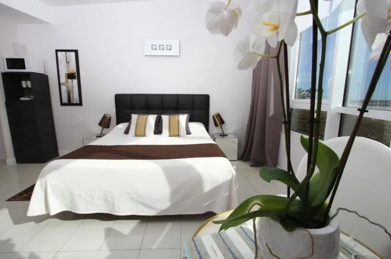 Une chambre lumineuse avec un grand lit recouvert d'une courtepointe blanche et de coussins.
