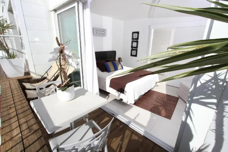 Une chambre lumineuse s'ouvre sur une terrasse avec mobilier blanc.