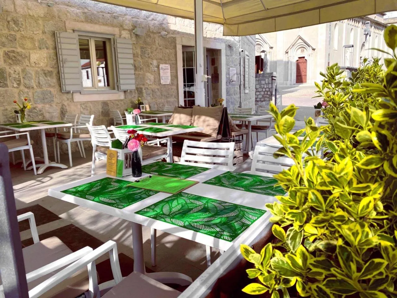 Tables et chaises disposées en extérieur sous une tonnelle ombragée.