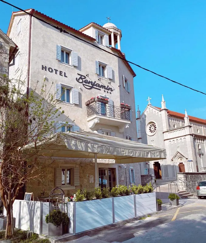 Façade d'un bâtiment blanc avec des fenêtres et des balcons, surplombant une terrasse ombragée.