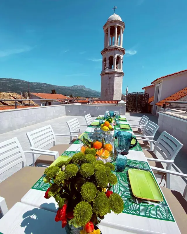 Table dressée avec des fruits et des fleurs sur une terrasse ensoleillée.