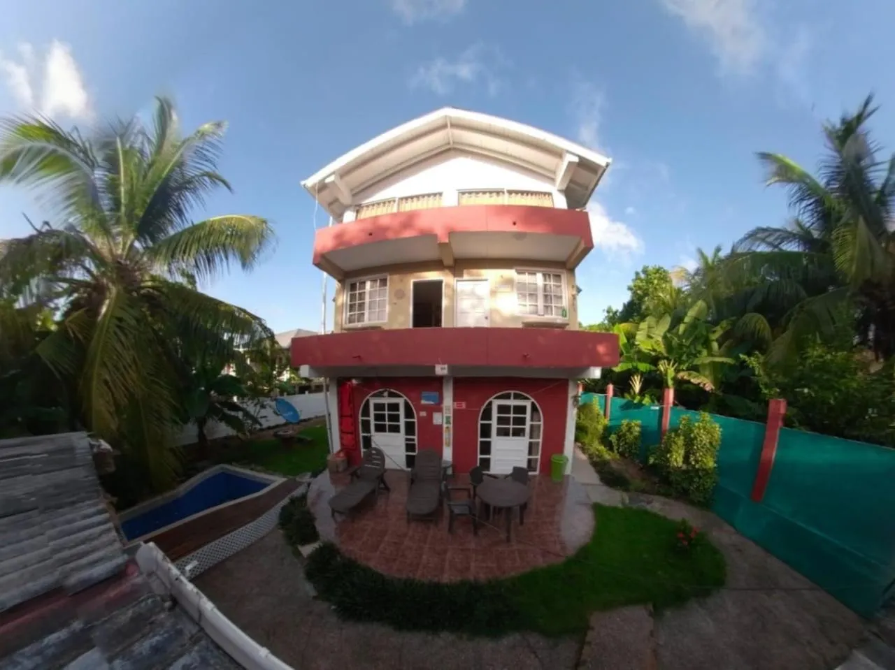 Bâtiment coloré à deux étages avec des palmiers et une petite piscine.