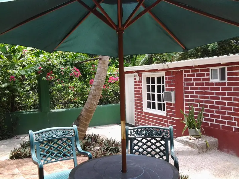 Une table et des chaises en fer forgé se trouvent sous un parasol vert près d'un bâtiment en briques.