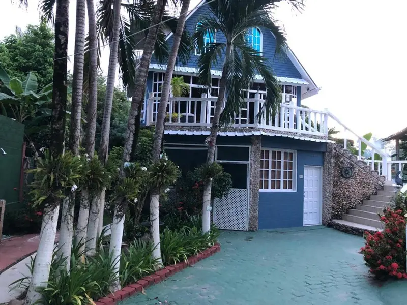 Bâtiment bleu à deux étages avec balcon et végétation tropicale.