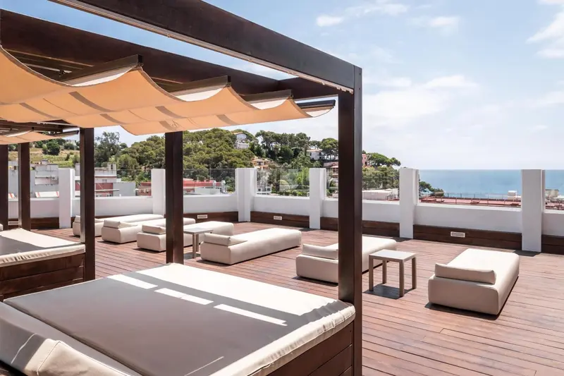 Terrasse aménagée avec des transats et des canapés blancs sous des pergolas.
