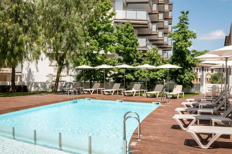 Une piscine rectangulaire bordée de transats blancs sous des parasols.