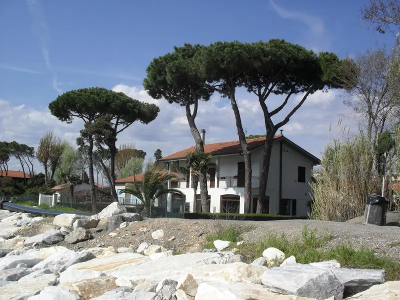 Bâtiment blanc à deux étages entouré de végétation et bordé de pierres.