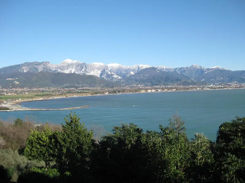 Vue panoramique sur une étendue d'eau turquoise bordée de montagnes enneigées et d'une ville côtière.