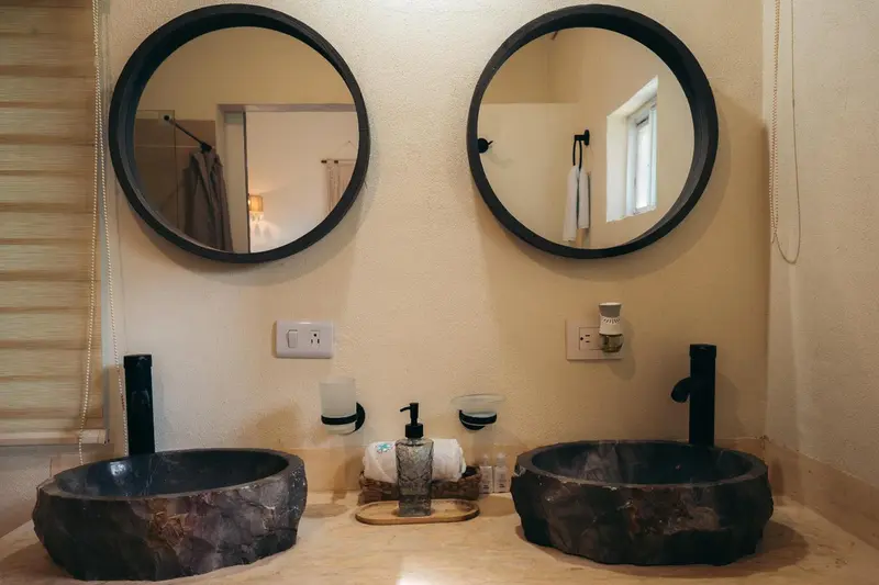 Une salle de bain avec deux vasques en pierre et des miroirs ronds.