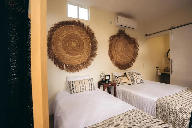 Une chambre lumineuse avec deux lits simples et une décoration murale en fibres naturelles.