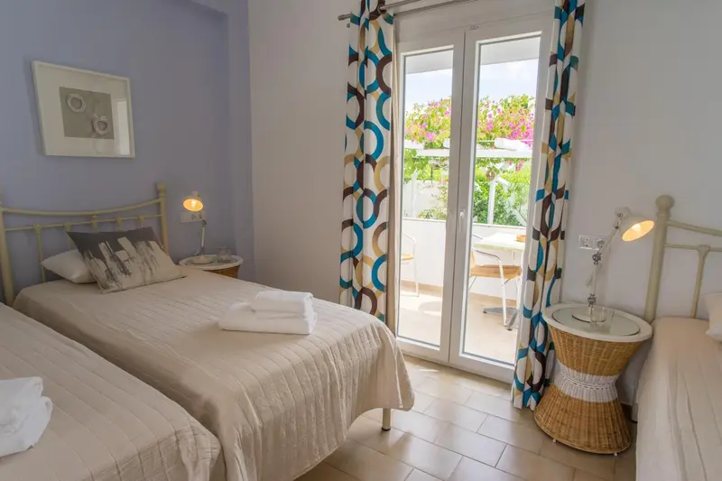 Chambre lumineuse avec deux lits simples et une porte-fenêtre donnant sur une terrasse.