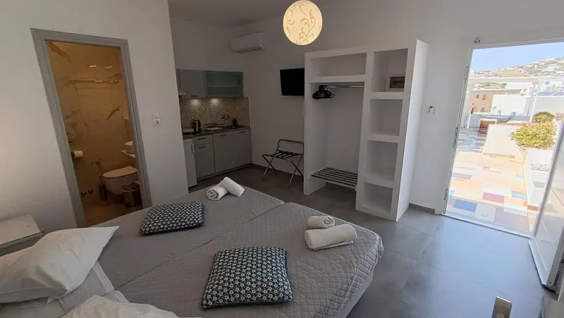 Une chambre lumineuse avec un lit fait et un espace cuisine.