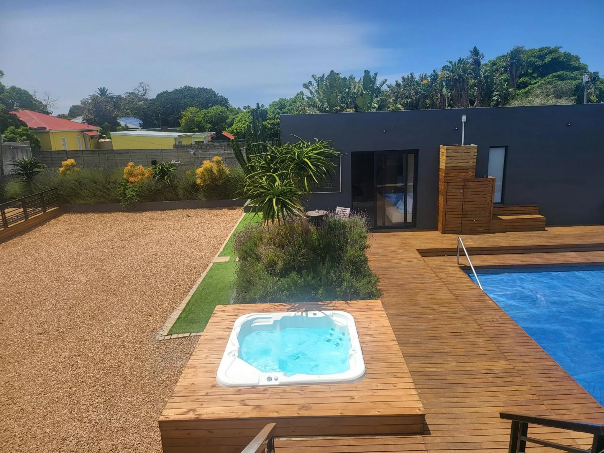 Terrasse en bois avec jacuzzi et piscine, devant un bâtiment moderne.
