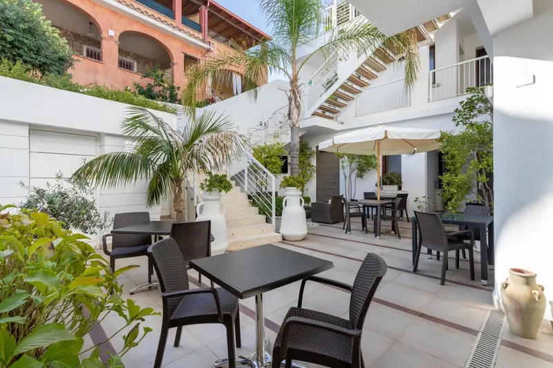 Terrasse ombragée avec tables et chaises près d'un bâtiment blanc.