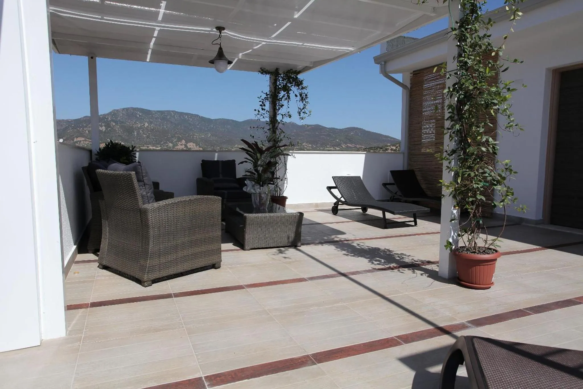 Terrasse ombragée avec mobilier de jardin et vue sur les montagnes.