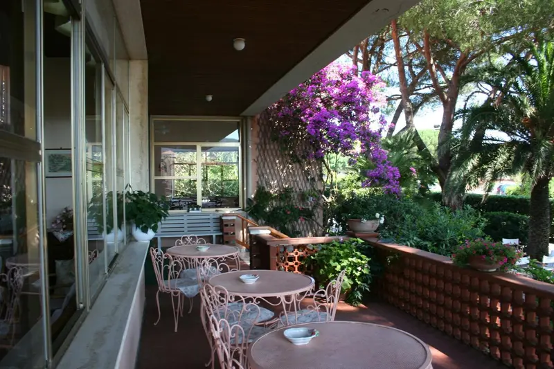 Terrasse ombragée avec tables et chaises en fer forgé, décorée de plantes fleuries.