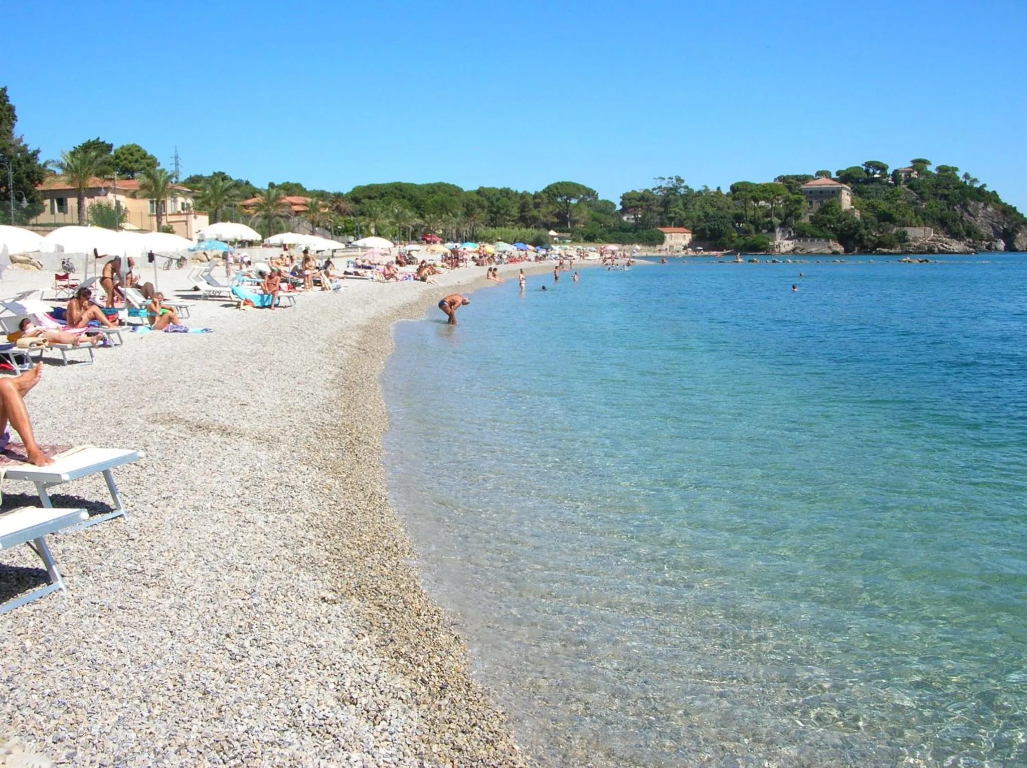 Une plage de galets avec des transats et des baigneurs dans une eau turquoise.