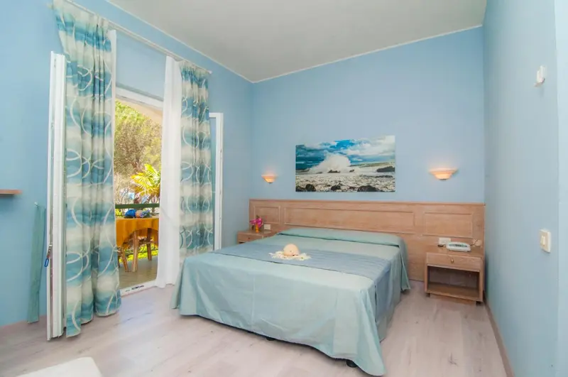 Chambre lumineuse avec un lit recouvert d'une couverture turquoise et un tableau représentant une scène marine.
