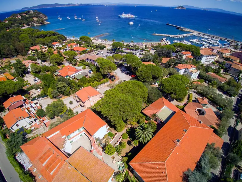 Vue aérienne d'un complexe hôtelier avec des bâtiments aux toits rouges et une végétation luxuriante, surplombant une plage et une marina.