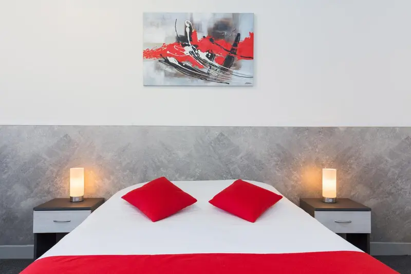 Une chambre avec un grand lit recouvert d'une couette blanche et de coussins rouges.
