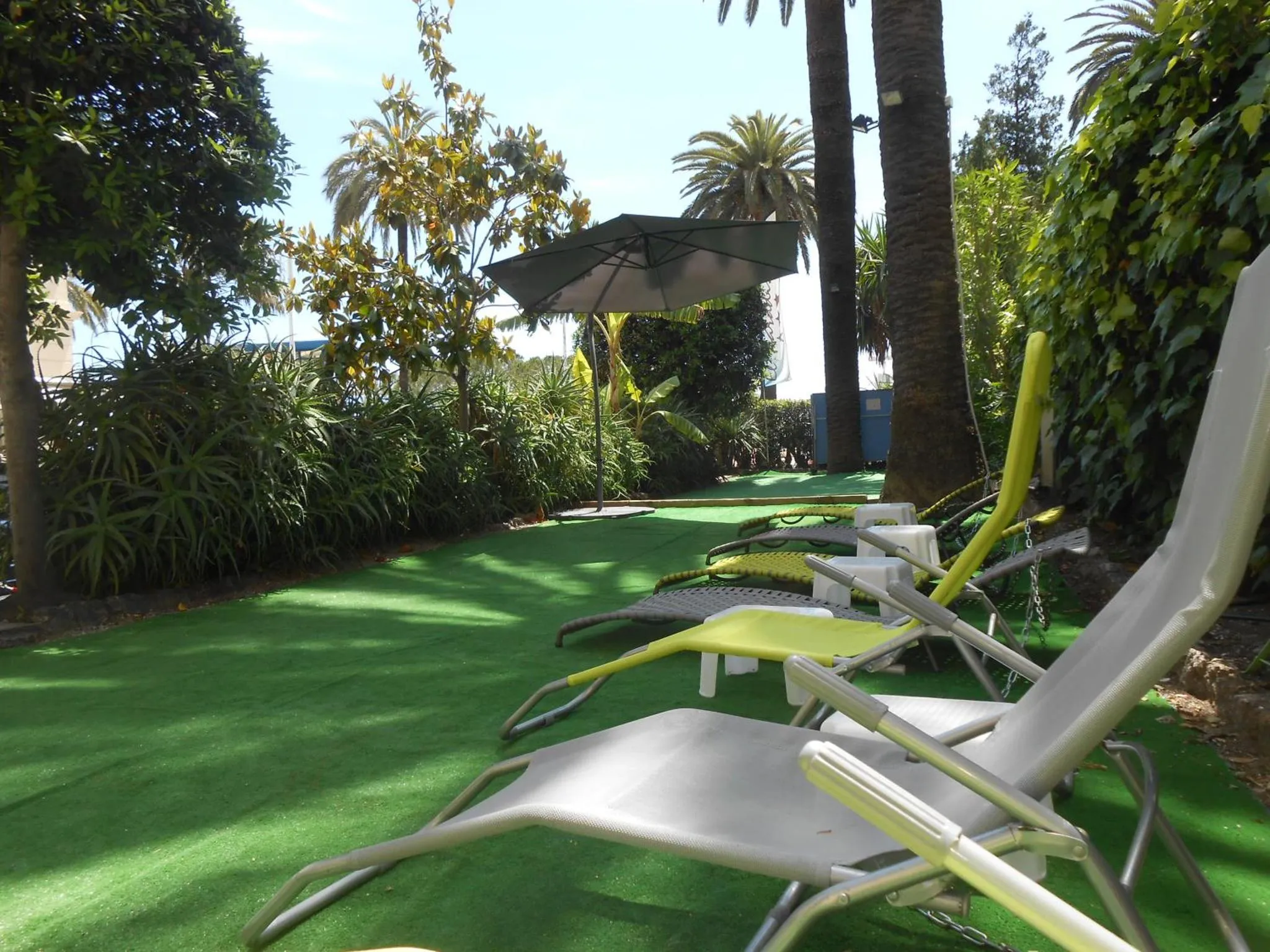 Transats verts et blancs disposés sur une pelouse synthétique dans un jardin tropical.