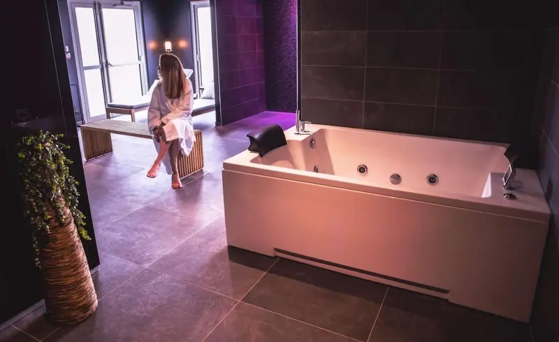 Une femme assise sur un banc près d'une baignoire dans une salle de bain lumineuse.