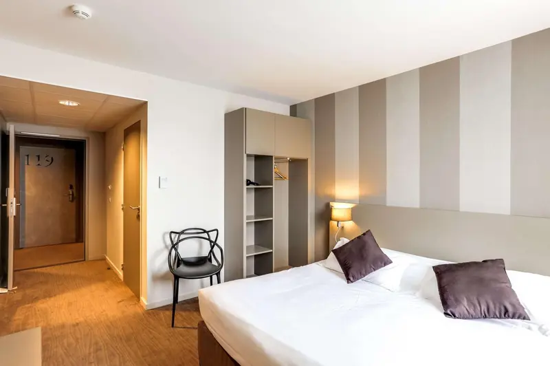 Chambre lumineuse avec un lit fait et un espace rangement.