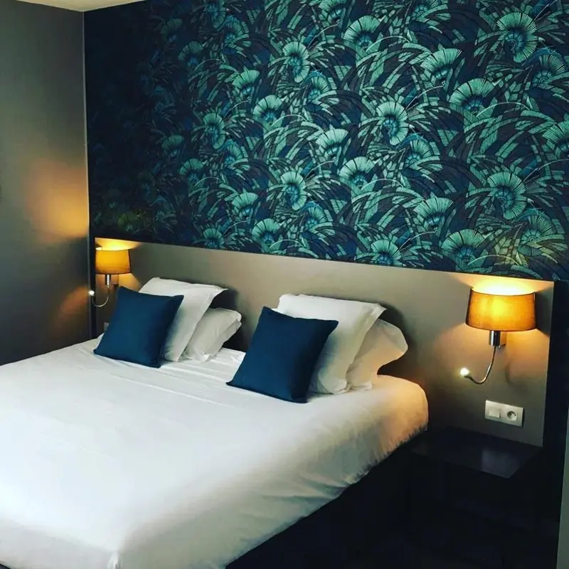 Un lit double avec des oreillers blancs et des coussins bleus devant un mur à motifs.