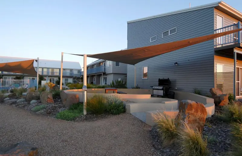 Terrasse ombragée avec mobilier de jardin et barbecue devant des bâtiments modernes.