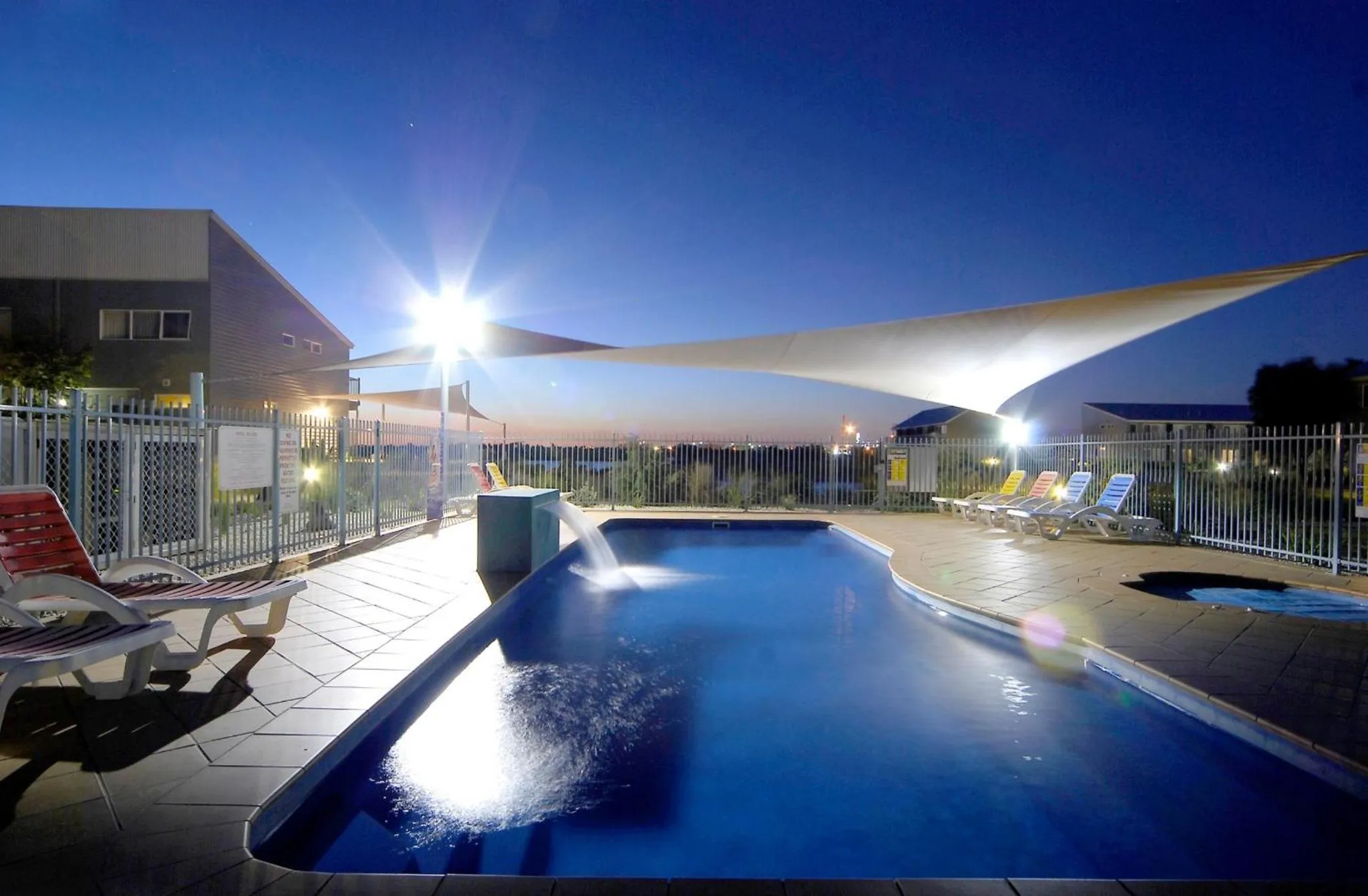 Une piscine illuminée au crépuscule avec des transats et une ombrelle.