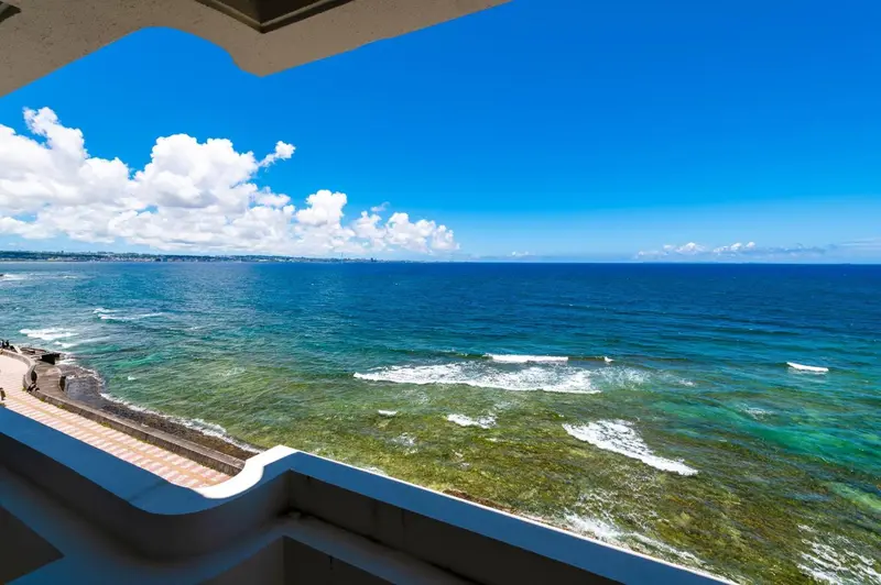 Vue sur l'océan bleu et le ciel nuageux depuis un balcon.