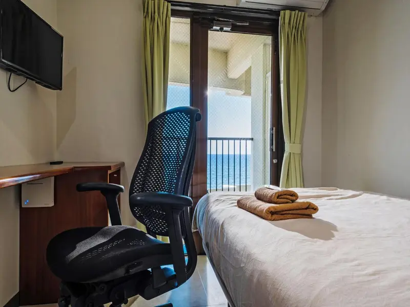 Une chambre lumineuse avec un bureau et un lit donnant sur une vue dégagée.