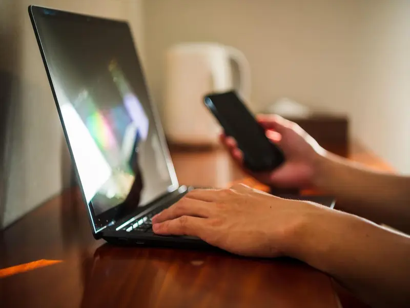 Une personne utilise un ordinateur portable et un téléphone sur une table en bois.
