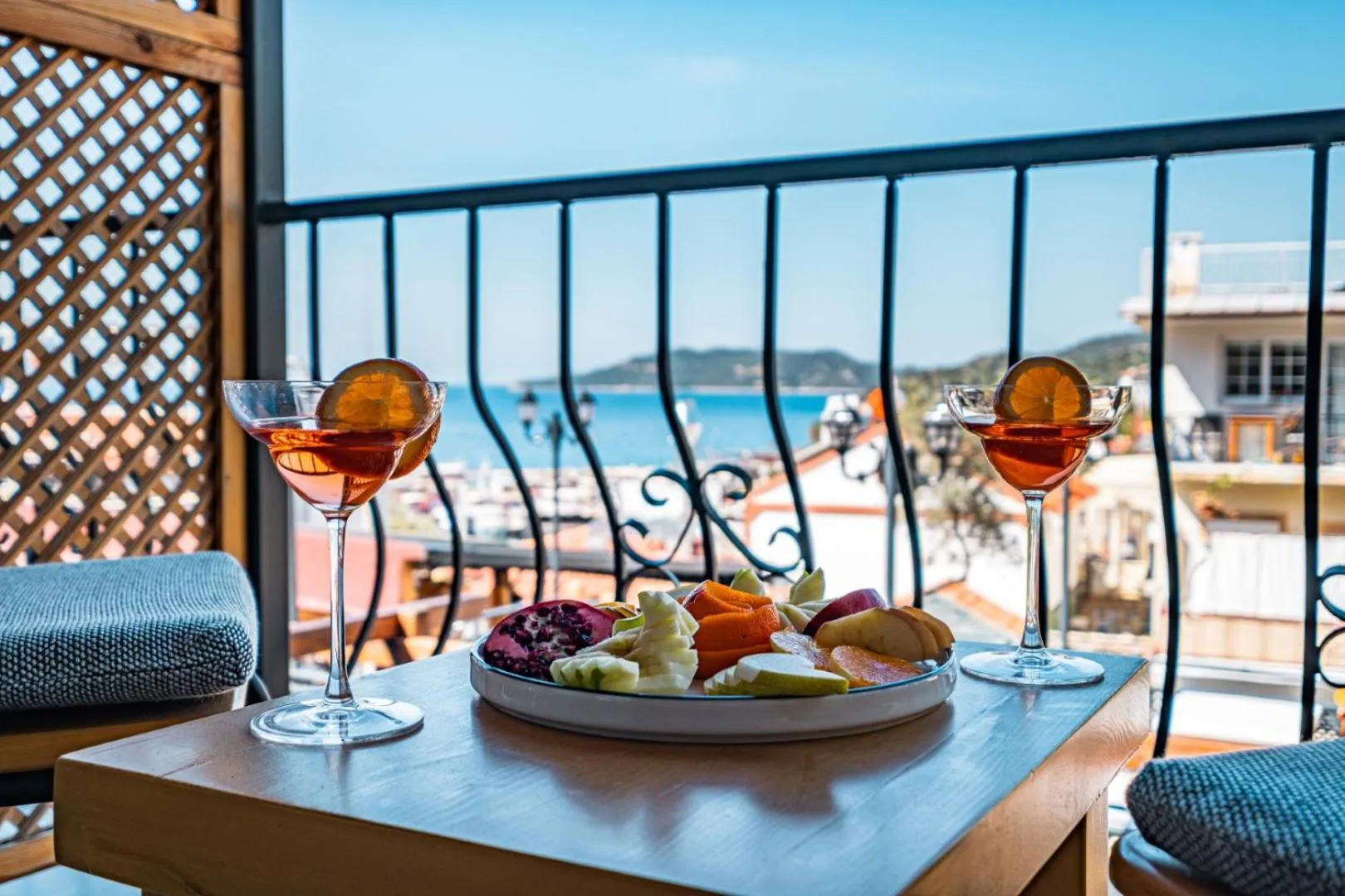 Deux verres de cocktail et une assiette de fruits sont posés sur une table sur un balcon avec vue sur la mer.