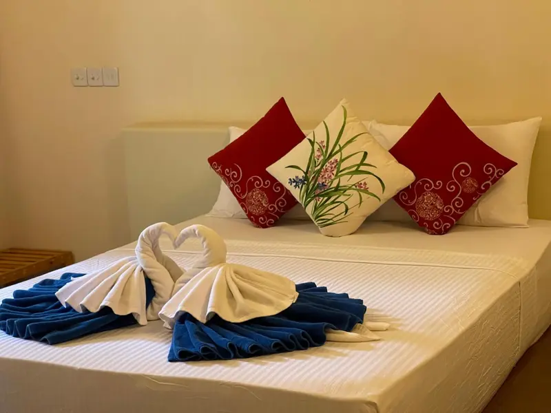 Un lit double est soigneusement fait avec des oreillers décoratifs et des serviettes en forme de cygne.