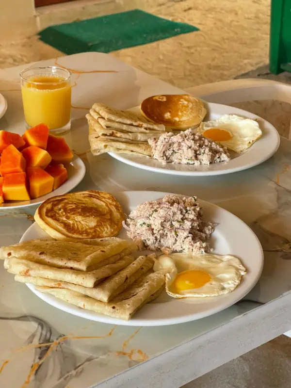 Une table est dressée avec un petit-déjeuner composé de fruits, d'œufs et de galettes.