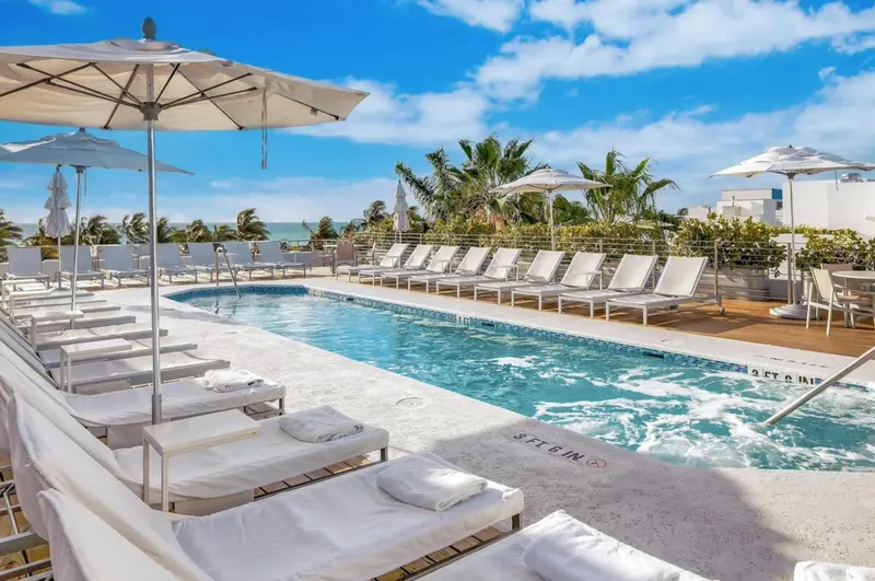 Transats blancs disposés autour d'une piscine rectangulaire sous des parasols.