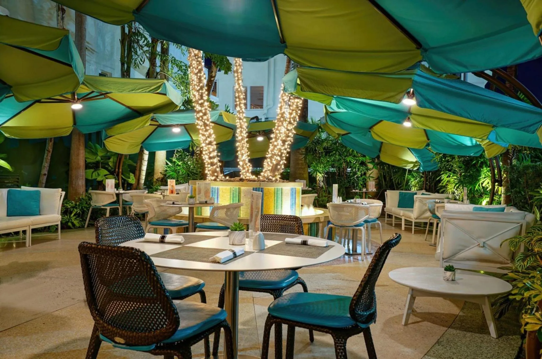 Tables et chaises disposées en extérieur sous des parasols colorés.