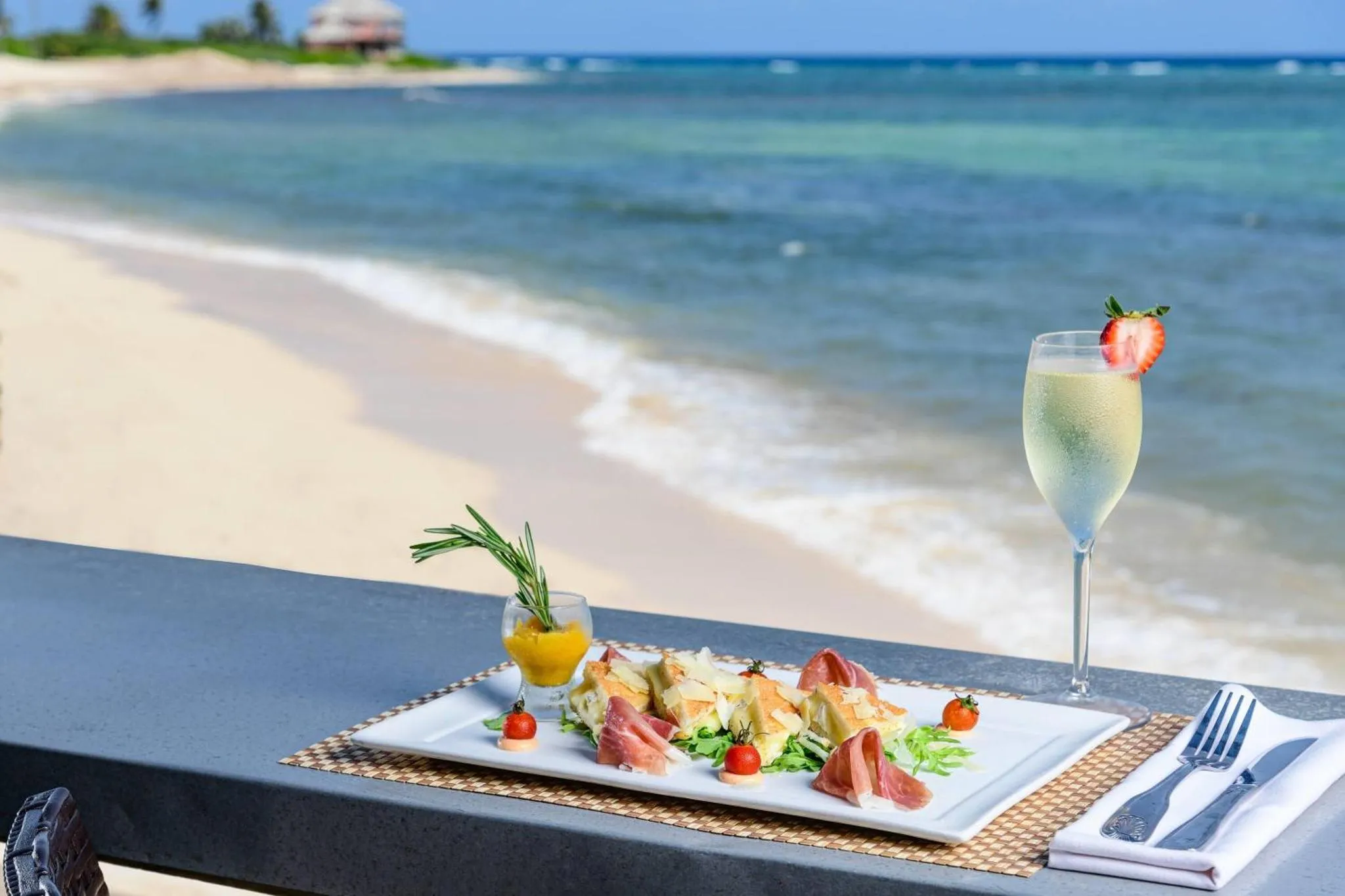 Un cocktail et une assiette de salade sont posés sur une table face à la mer.