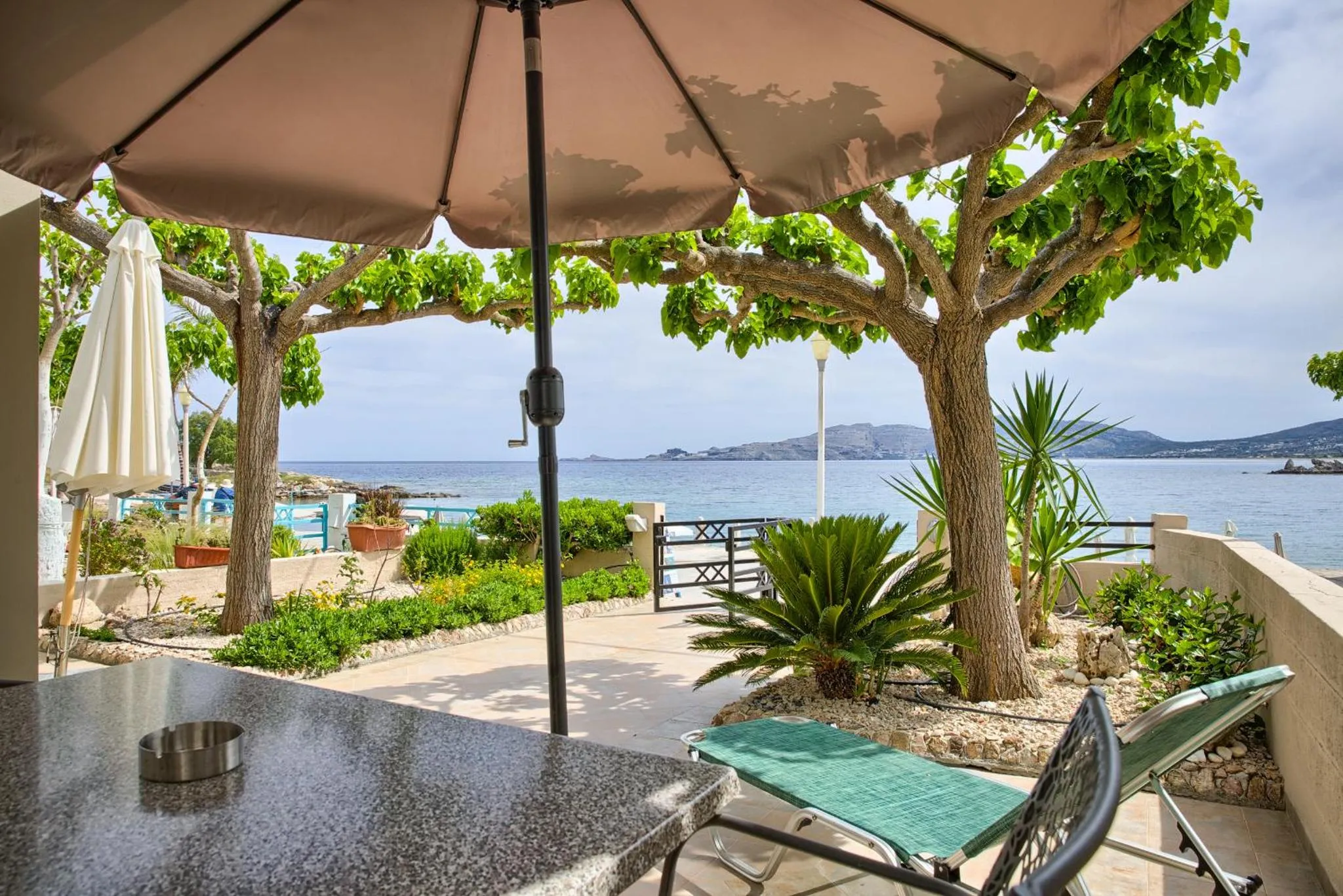 Terrasse ombragée avec table et transat face à la mer.