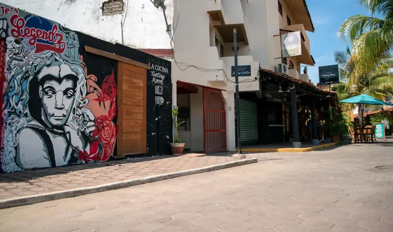Façade d'un bâtiment blanc avec une fresque murale colorée et des ouvertures sombres.