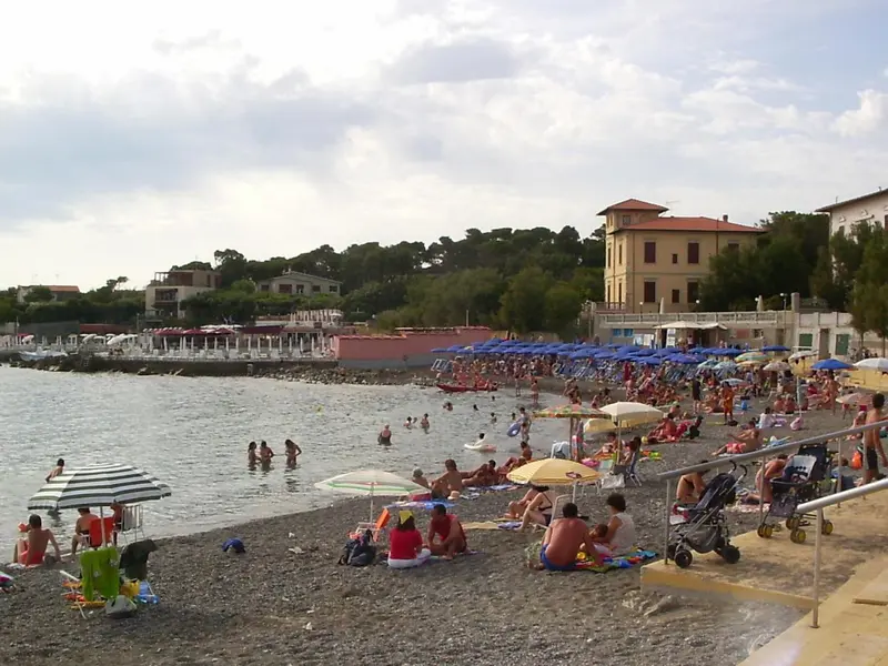 Une plage de galets animée avec des baigneurs et des parasols colorés.