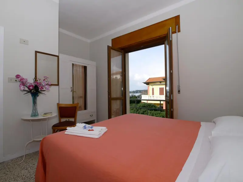 Une chambre lumineuse avec un lit recouvert d'une couverture orange et un balcon ouvert.