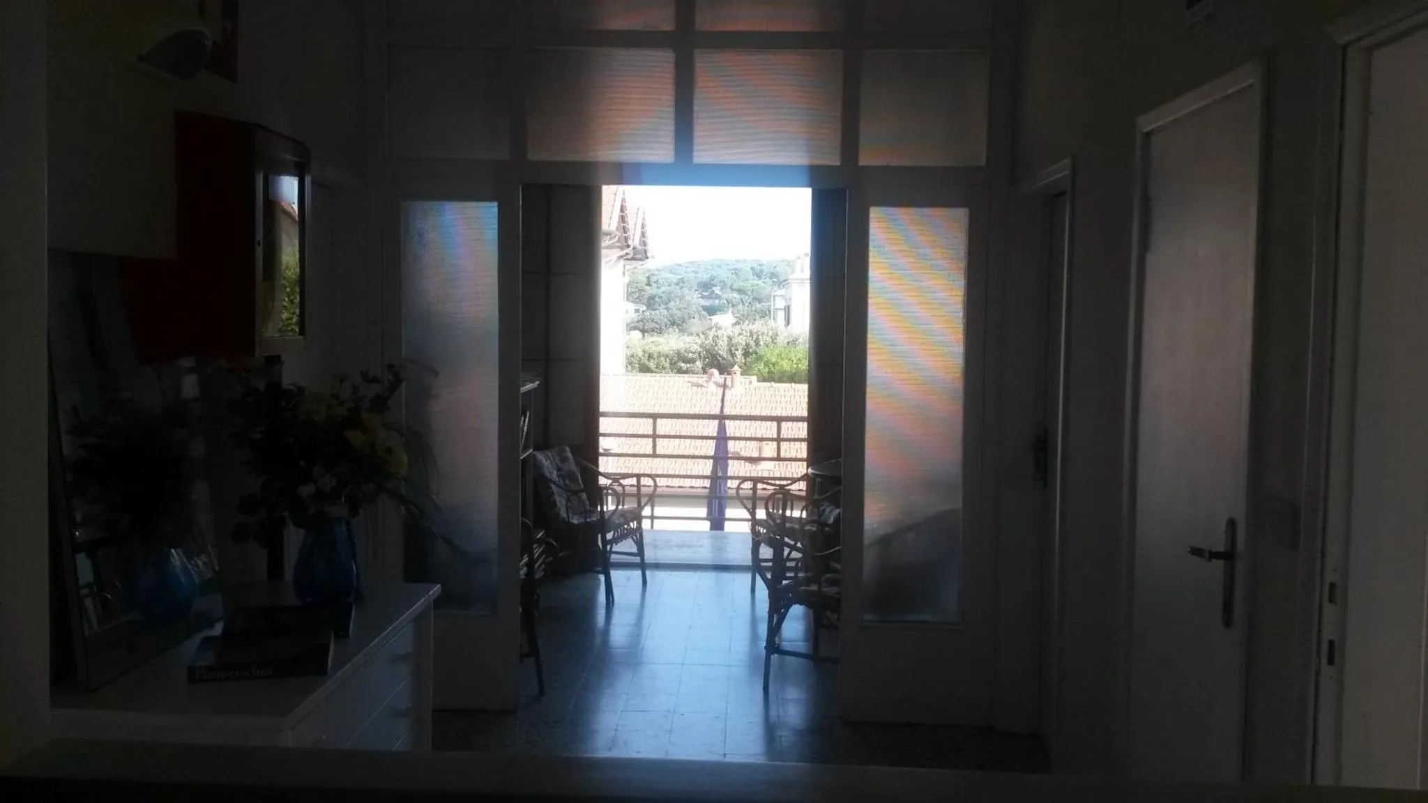 Vue sur une terrasse ensoleillée depuis un intérieur sombre.